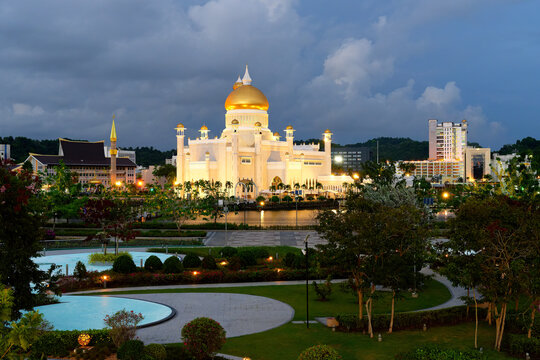Omar Ali Saifuddien Mosque stands illuminated at dusk in Bandar Seri Begawan, Brunei with surrounding gardens and city skyline