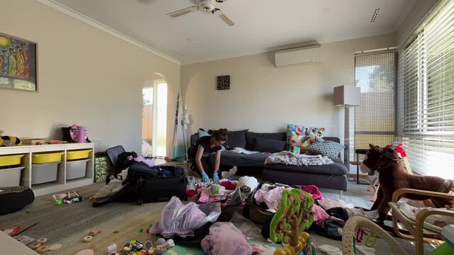 Time lapse of a young woman picks up toys and clothes from the floor in a living room. She organizes items and tidies space