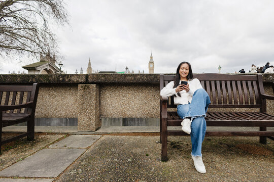 Smiling Woman exploring London using smartphone on bench