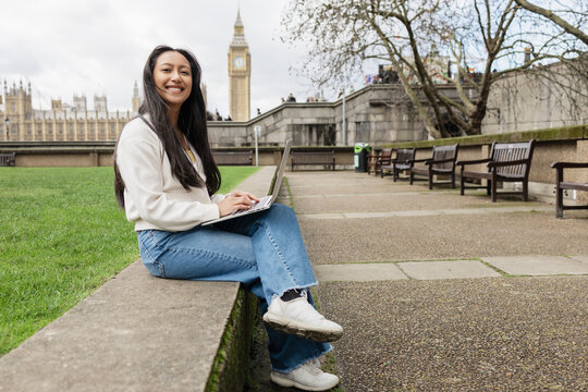 Smiling remote worker using laptop outside Parliament in London
