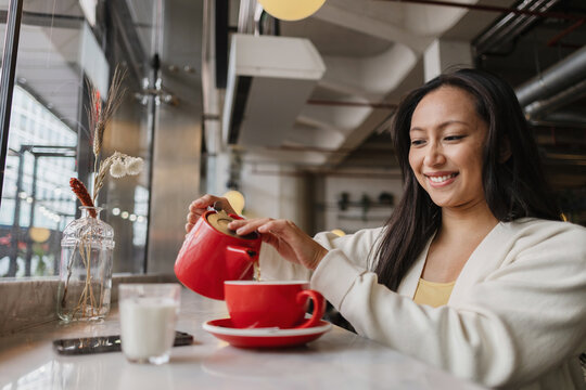 Woman smiling, pouring tea from red pot into cup
