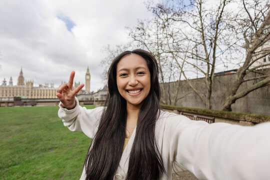 Smiling traveler taking selfie with peace sign in London