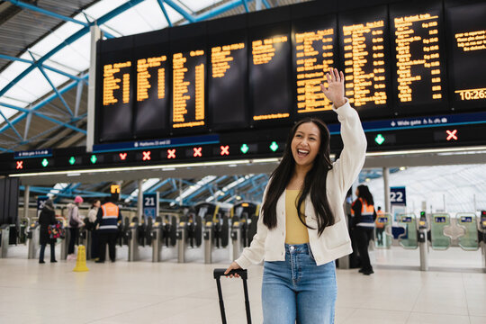 Happy Woman traveller waving at train station departure board