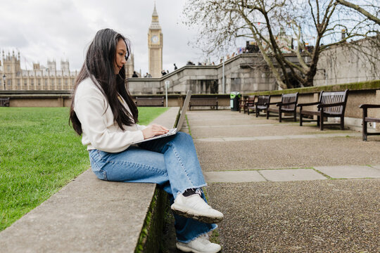 Asian Woman working remotely on laptop in London park