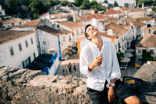 Person Enjoys Ice Cream While Sitting on a Wall in a Quaint Town