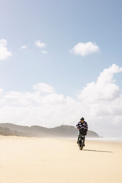 Man riding e bike along empty beach under cloudy sky