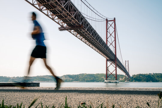 Runner Crosses Under Bridge Near Water in Summer Morning Light