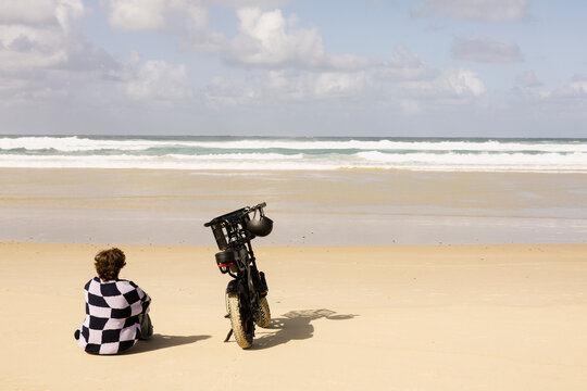 Man sitting with e bike on beach and watching ocean waves