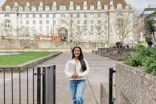 Woman smiling student carrying laptop walking in London