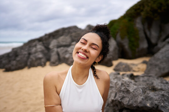 Woman smiling with closed eyes enjoying beach rocks