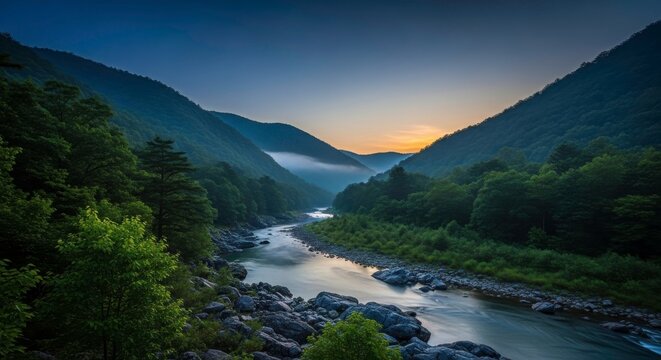 Winding river flowing through a deep mountain valley at sunrise with fog and green forest slopes