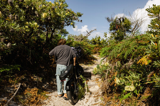 Man pushing e bike along sandy path through coastal bush with banksia