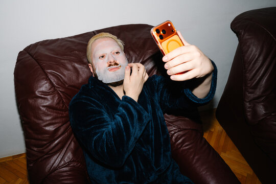 Man Wearing Sheet Mask and Looking at Smartphone