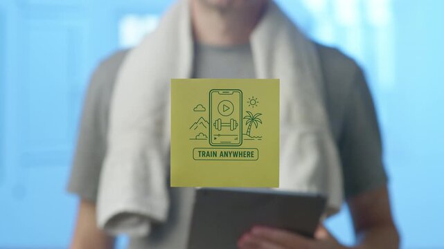 Fit man with a towel around his neck holding a tablet while a sticker promoting a fitness app with the slogan train anywhere is placed on the foreground glass, symbolizing remote workouts