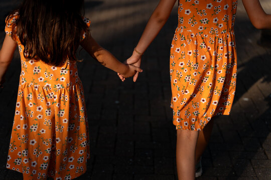 Sisters Walking Hand in Hand in Flower Dresses in Summer