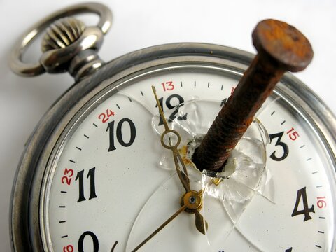 Broken pocket watch with nail through face, cracked glass and damaged clock mechanism, isolated on white background