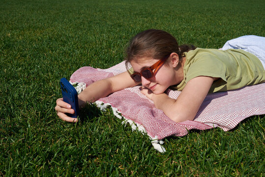 Girl lying on grass looking at phone in sunny park