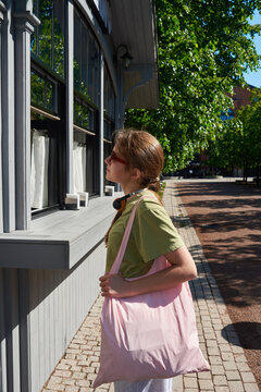 Teenager with pink tote bag observes menu of outdoors cafe