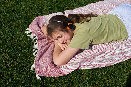 Girl listens to music while lying on a blanket on the grass 