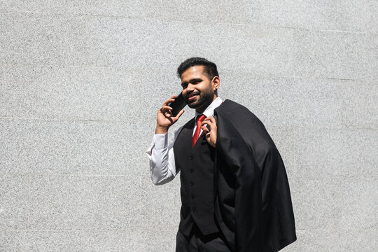 Smiling Indian man talking by mobile phone against grey wal at street.
