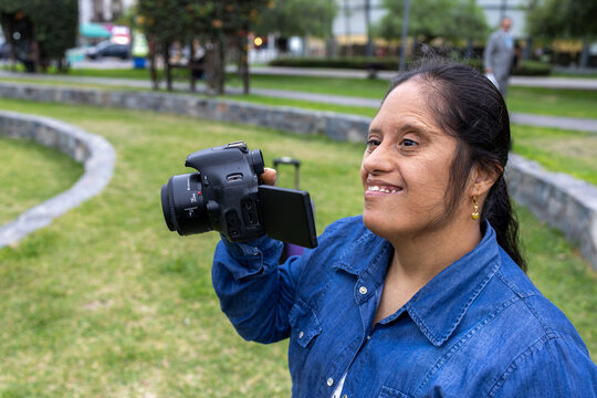 Portrait of a confident woman with Down syndrome carrying a mirrorless camera outdoors