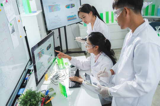 Laboratory scientist research computer analysis data teamwork experiment with Asian adult team in white coat studying chart, sample, glassware inside modern clinic lab