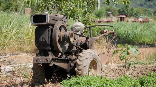 Old farm machine with large wheels stands in a grassy field near trees and distant buildings. Small-scale farming.