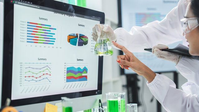 Laboratory scientist research data monitor chart analysis beaker, focused chemist examining green liquid sample beside digital report screen in modern medical lab