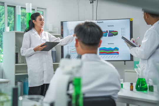 Scientist laboratory presentation research chart team meeting experiment data screen group reviewing result during collaborative chemistry briefing with glassware and microscope