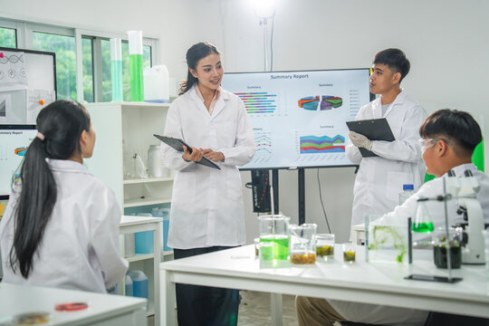 Laboratory student scientist presentation research teamwork white coat tablet chemistry classroom, focused young adult group discusses chart data during experiment training in modern science lab