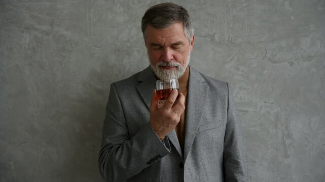Handsome and successful businessman in stylish suit holding glass whiskey while sitting on the stool