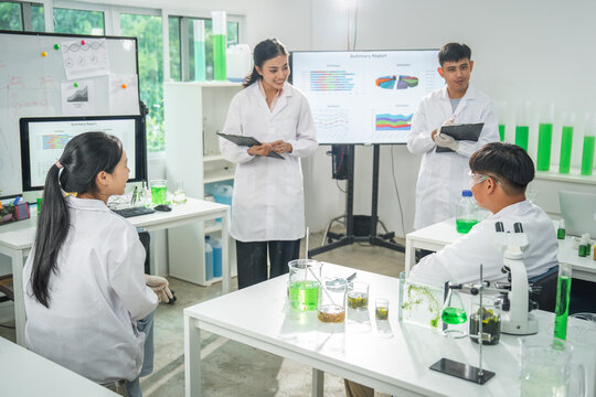 Laboratory student scientist chemistry experiment classroom beaker microscope group in white coat discuss green liquid research during science lesson with chart display and glassware