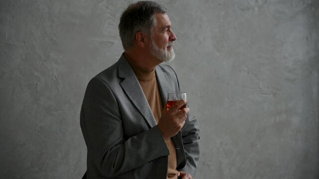 Handsome and successful businessman in stylish suit holding glass whiskey while sitting on the stool