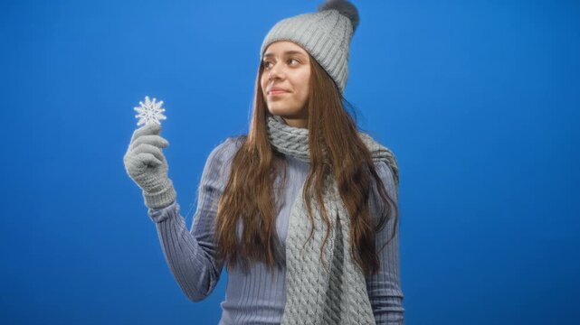 Woman holding snowflake ornament in gloved hand, wearing beanie scarf and ribbed sweater, looking sideways in studio; quiet wonder.