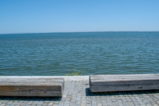 Tranquil Waterfront Scene with Wooden Benches and Distant Pier under Clear Blue Sky