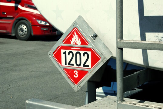 Flammable 1202 class 3 placard on rear of tank trailer with red truck in background.