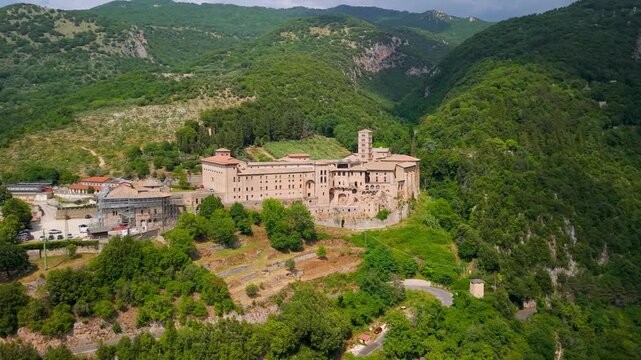 Santa Scolastica Monastery Subiaco Italy 4K Drone. Aerial panning left to right view of historic abbey on mountain cliff and valley opening to town. Sacred landmark scenery b roll cinematic video