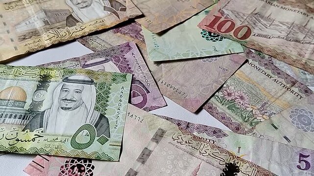 A close-up of Saudi Riyal (SAR) banknotes arranged on a white background, showing various denominations.