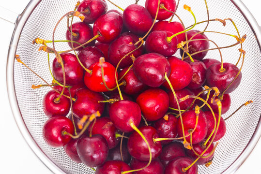 Ripe cherries in a colander on a white background