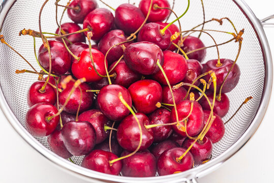Ripe cherries in a colander close up on a white background