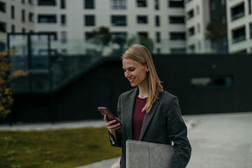 Fototapeta premium Businesswoman checking smartphone while walking outside office building