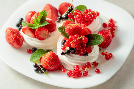 Pavlova dessert with fresh berries and mint on a white plate.