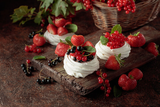 Pavlova dessert with fresh berries and mint on an brown vintage table.