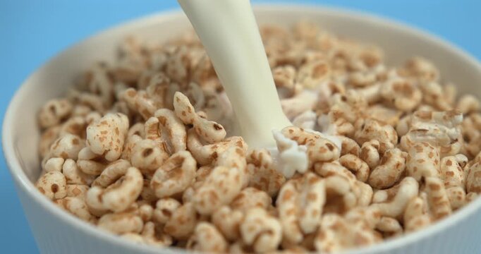Milk pouring into crispy puffed honey wheat cereal in bowl creating dramatic splash in super slow motion