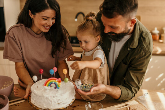 Family celebrating birthday with daughter decorating cake in kitchen