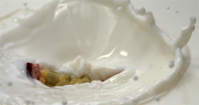 Passion fruit slice falling into milk or cream with splash in super slow motion