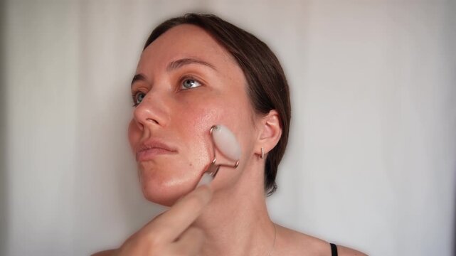 Woman using a stone facial roller for face massage and daily skincare against a neutral background