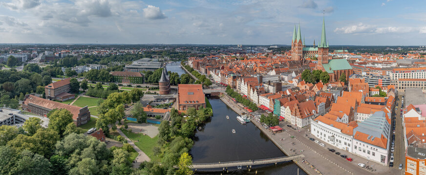 Historic city center of L&uuml;beck, Germany with medieval Holstentor gate, Trave river with boats, traditional brick gothic architecture, and spires of St. Marien church.