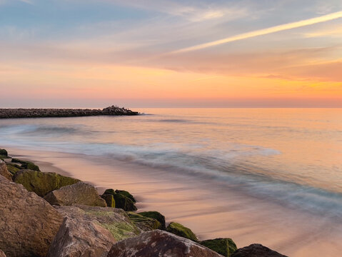 Serene sunset over the Atlantic at Praia do Furadouro  in Ovar, Portugal, with glowing orange skies reflecting on the wet sand and mossy rocks