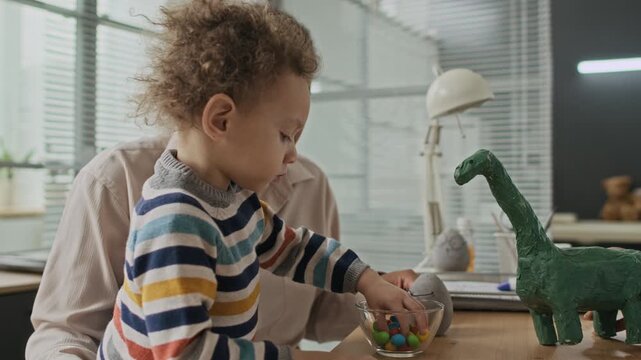 Biracial woman and young child studying green dinosaur model at desk during doctors appointment in clinic. Ideal for promoting early childhood education, creative learning, or parenting programs